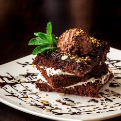 Chocolate brownie cake with a scoop of ice cream with a mint leaf on a white plate